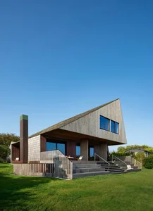 A modern house with a boat-like design, featuring a large deck and stairs, with two rooms on either side, surrounded by natural light and warm wooden exterior walls