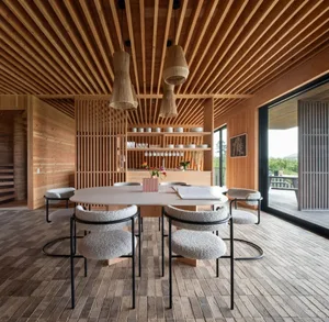 Warm and inviting open concept dining space with a pink vase, a dining table, chairs, a kitchenette, and ample seating options