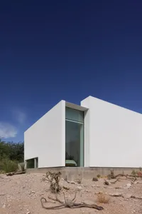 Open living area with a large white wall, two windows, and natural light