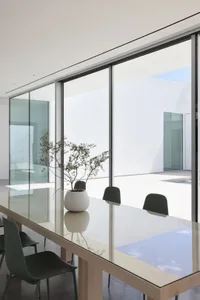 A well-lit dining area with a glass table surrounded by chairs, a vase, and a comfortable atmosphere