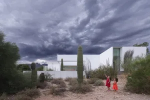 A tranquil outdoor space with a white building and a cactus garden, featuring young girls playing near the plants