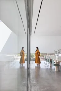 Two women standing in front of a glass wall in a dining room with chairs and a potted plant, reflected in the mirrored surface