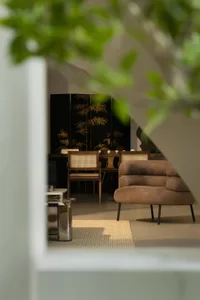 Cozy living space with a brown couch, chairs, and a dining table, lit by natural light from a window