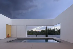 A modern pool area with a large pool surrounded by white walls, potted plants, and a minimalist design