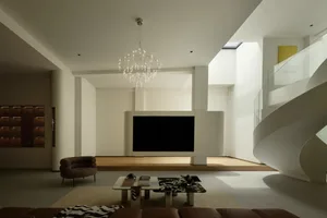 Sleek modern living space with a flat screen TV, chairs, couches, and dining tables, surrounded by neutral tones and minimal decoration