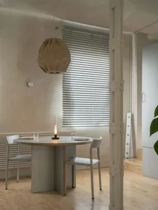 Modern living space with white walls, wooden floors, and large windows, featuring a dining table, chairs, and a potted plant