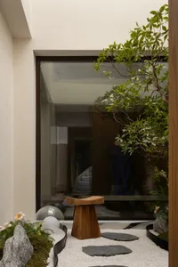 A well-lit living area with a large window, potted plants, vases, and a chair, creating a warm and inviting atmosphere