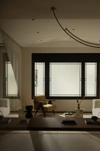 A modern living area with two couches, a chair, and a dining table, surrounded by white walls and natural light from a large window