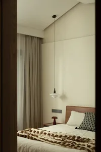 A serene bedroom with a white wall, wooden headboard, and a chair, featuring a cozy bed setup with two pillows