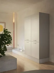 A minimalist bathroom with white fixtures, a large cabinet, sink, and toilet, with two potted plants adding a touch of greenery