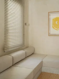 A living room with a couch and bench next to each other, surrounded by white walls, two windows, and wooden furniture