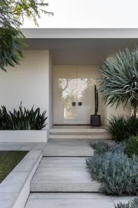A white house with a large doorway leading to a patio area, surrounded by potted plants and a cactus, creating a comfortable and inviting living space