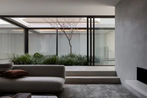 A bright and inviting living area with a gray couch, large windows, and potted plants