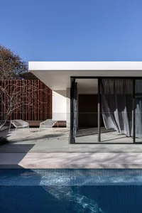 A modern house with a white concrete exterior and a pool in front, featuring two chairs and a relaxing atmosphere