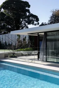 Modern house with glass walls, a pool, and outdoor seating areas, surrounded by a calm and inviting atmosphere
