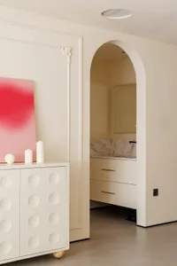 A clean and well-organized all-white bathroom with two vases on the countertop near the sink and mirror