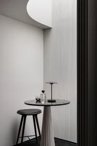 A small table with a vase sits in front of a striped wall, surrounded by two chairs in an elegant and well-organized interior design space