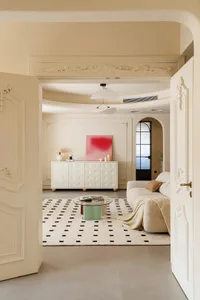 Cozy open living space with a white couch, two chairs, a dining table, and a vase, surrounded by books and natural light