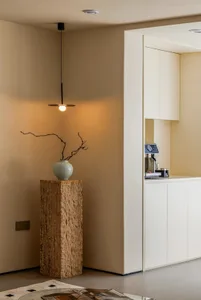 A minimalist interior space with a white wall, a wooden stand, a vase with a branch, and two cups and a bottle on a simple surface