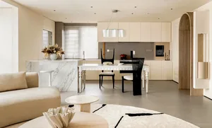 Open modern kitchen and dining space with white marble countertops, a large island dining table, and a comfortable couch in the adjacent living area