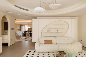 Cozy modern living area with a white couch, black and white checkered rug, and a dining table, set in a room with circular walls and two chairs