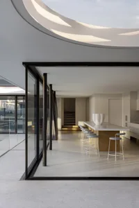 Open living area with a modern and minimalistic design, featuring white walls, wooden floors, a dining table, chairs, and a bowl on the table