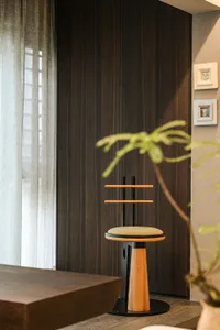 A wooden chair sits in front of a window with two potted plants on either side, surrounded by three framed pictures on the wall