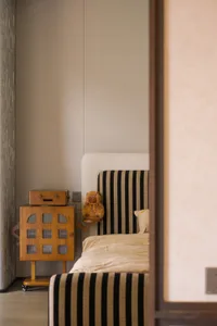 A cozy bedroom with a bed featuring a striped blanket, a small table, and two teddy bears, creating a warm and inviting atmosphere