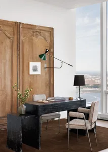 Well-lit living area with a wooden door, desk, chair, and lamp, creating a cozy atmosphere for relaxation or work