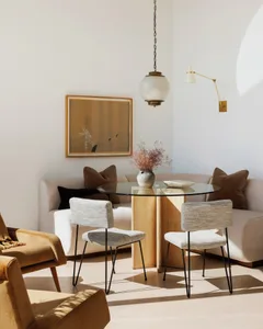 Open living area with a large couch, two chairs, and a dining table made of wood and leather, surrounded by natural light