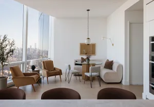 Architectural rendering of a high-rise living room with white walls, hardwood floors, and large windows offering a city view, featuring two couches, chairs, a dining table, and decorative accents