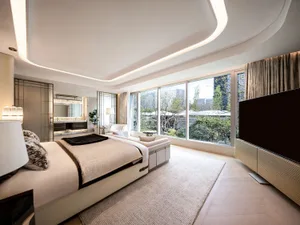 A comfortable living room with a white bed, black headboard, and natural light from windows, surrounded by couches and a TV