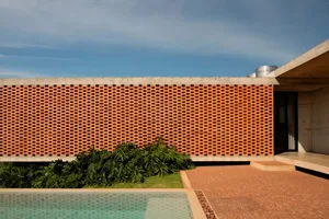 Exterior view of a simple building with an orange brick wall and a large window, set against a neutral background