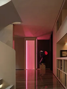 A modern hallway with concrete walls, a large statue on a pedestal, and two pink lights adding warmth to the space