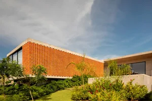 A modern building with a unique orange brick facade, large window, and surrounding potted plants