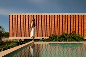 A woman stands on a bridge overlooking a reflective outdoor pool, surrounded by a scenic landscape