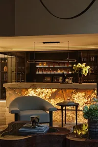 A luxurious living space with a wooden bar, dining table, and wine glasses, surrounded by vases and a sophisticated atmosphere