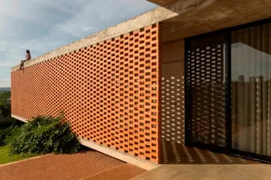 A modern architectural building with a unique checkered pattern on its exterior wall, made of orange bricks, with windows suggesting interior spaces