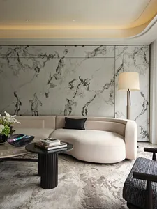 Modern living room with a large couch, marble tiles, a black coffee table, vases, and books, exuding sophistication and comfort