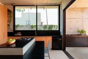 Modern kitchen with black countertops, a sink, chairs, a dining table, and a refrigerator, featuring a sleek and functional design