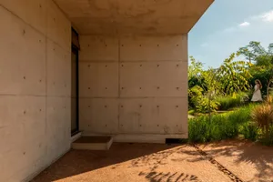 A modern concrete building with a large window on its side, set against a serene background with a tree nearby