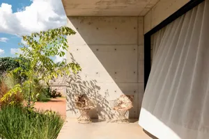 A relaxed outdoor patio with two chairs on a concrete surface, surrounded by potted plants and natural surroundings