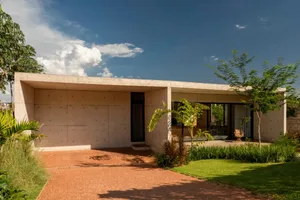 A modern house with a concrete exterior, large windows, and a comfortable living area with several chairs, filled with natural light