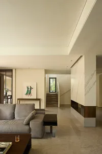 Modern living room with a couch, chair, dining table, and potted plants, surrounded by white walls and minimal decoration