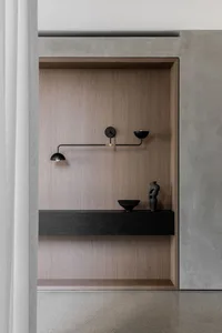 A modern bathroom featuring a wooden cabinet with a black shelf and two bowls, a lamp, and a minimalist design