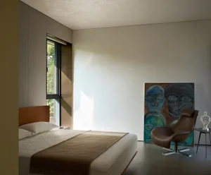 A well-lit bedroom with a large bed, two chairs, and a painting above the bed, set against a bright and inviting background