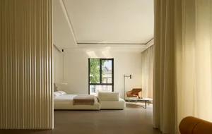 Open living area with a white couch near a window, a chair, and a dining table in a modern and minimalistic space with clean lines and neutral tones