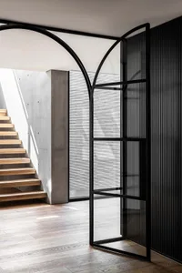 A modern home interior with a black doorway leading to a wooden staircase, featuring a glass panel for natural light and an elegant atmosphere