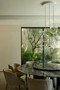 Dining area with a glass table surrounded by chairs, a potted plant, and natural light from a window