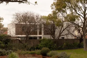 A modern house with a white exterior and a brick wall surrounding the backyard, featuring a living room and kitchen with a dining table and chairs